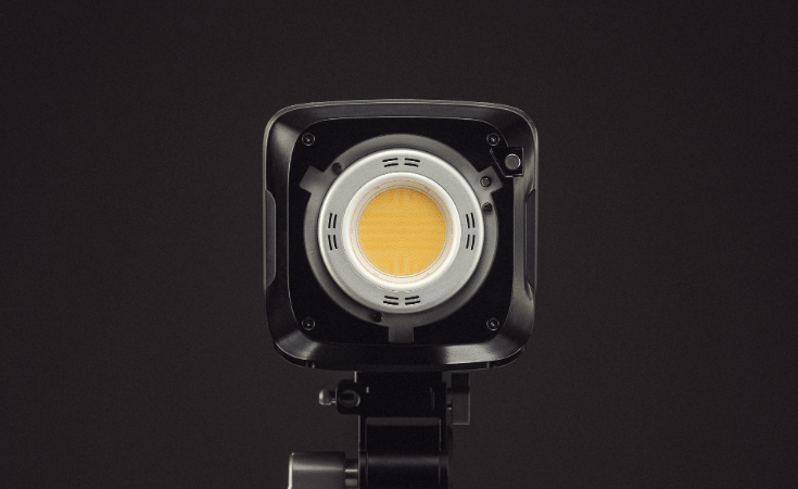 A professional COB LED studio light with a reflector emitting a warm golden glow.