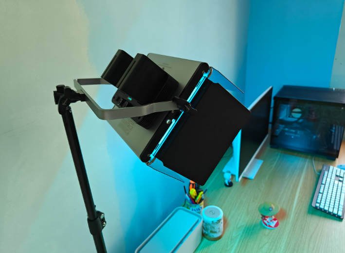 LED video panel light with barn doors mounted on a stand in a home office setup, paired with a computer and keyboard, showing its practical use for YouTube vlogging and remote work.